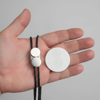 Hand holding a leather bracelet with a silver clasp and a round white object.