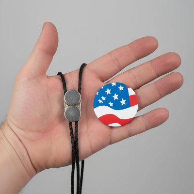 Hand holding a necklace with an American flag pendant against a gray background