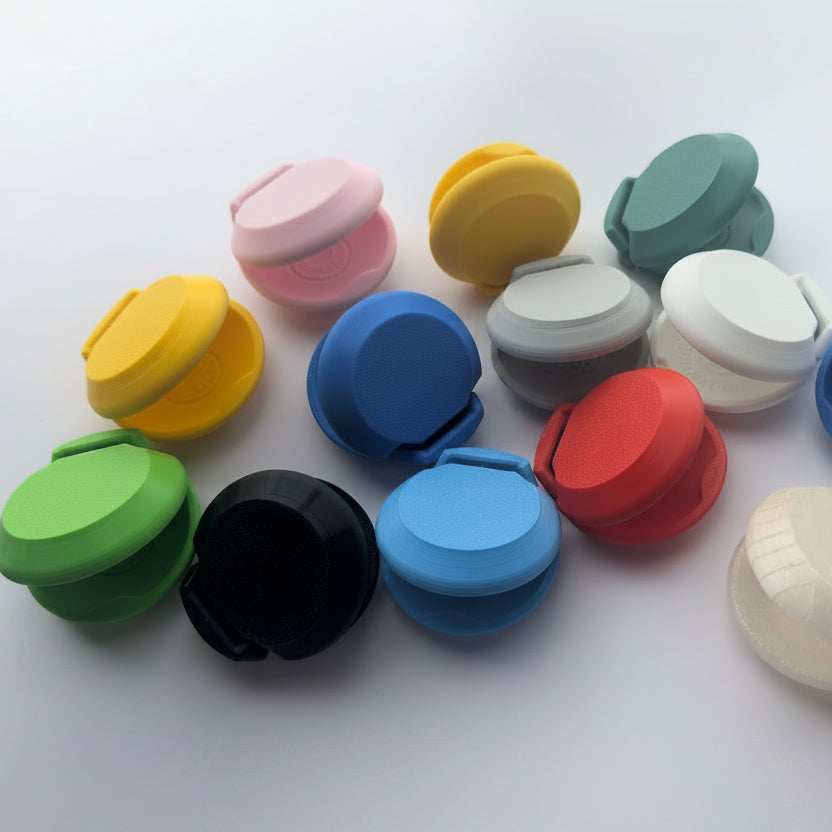 A group of small plastic castanets in multiple colors, including pink, yellow, green, black, blue, gray, red, white, and mint green, arranged on a plain light background.