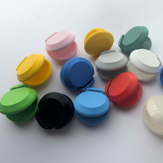 A group of small plastic castanets in multiple colors, including pink, yellow, green, black, blue, gray, red, white, and mint green, arranged on a plain light background.