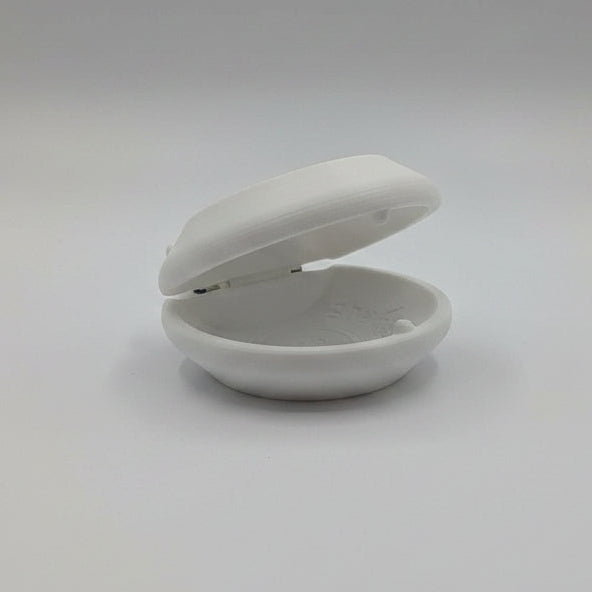 A white 3D-printed castanet shown open on a white surface, with several other colored versions in the blurred background.