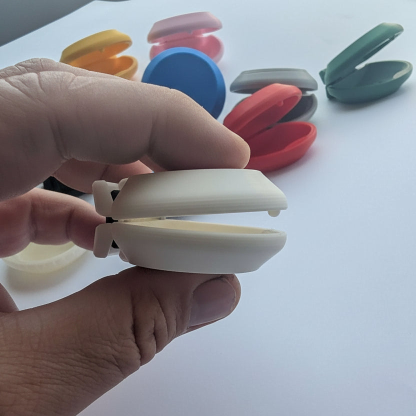 A hand holding acastanet with several other colorful castanets blurred in the background on a white surface.