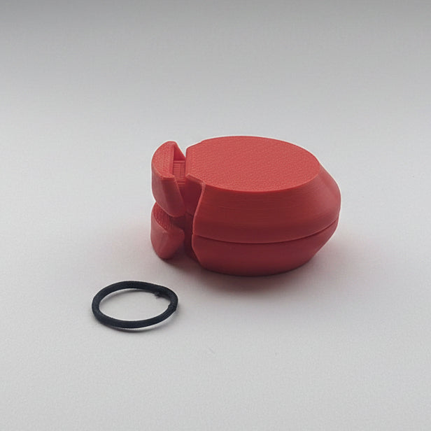 A red castanet with a small elastic band placed below it on a plain light background.