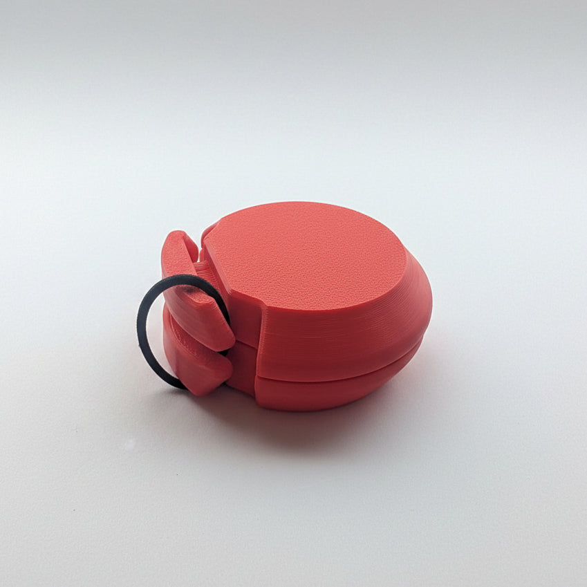 A red textured plastic castanet with elastic band, photographed on a plain white surface.